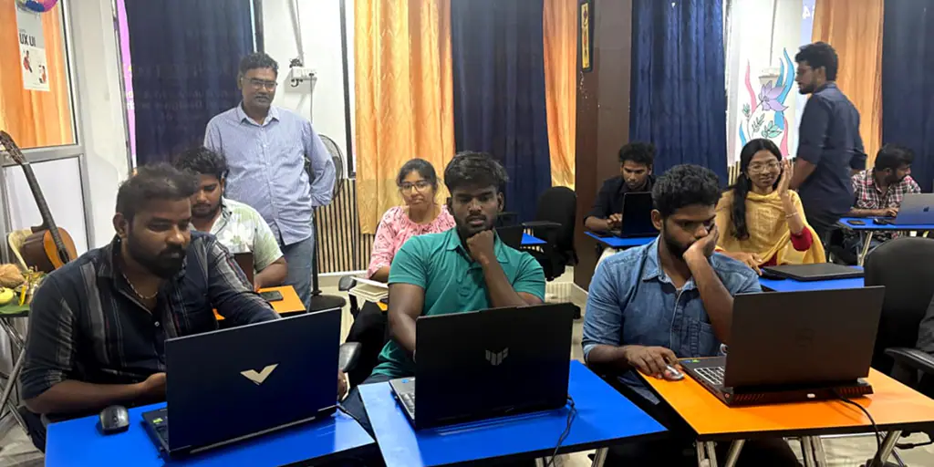 Students practising UX UI design on laptops while a mentor guides the class